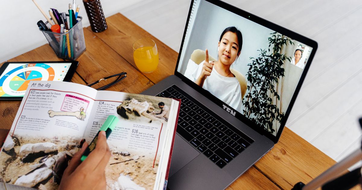 Personne suivant un cours en ligne sur un ordinateur portable avec un cahier d’exercices ouvert