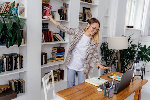 A young woman with earphones video conferencing from her home office surrounded by books.
