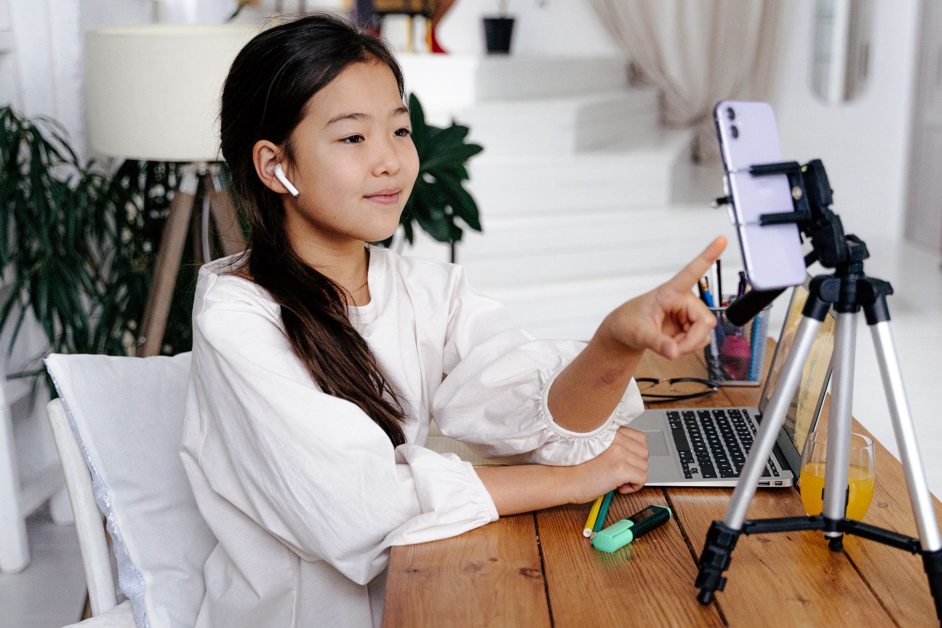 Asian girl using laptop and smartphone for video chat at home, engaging with device.