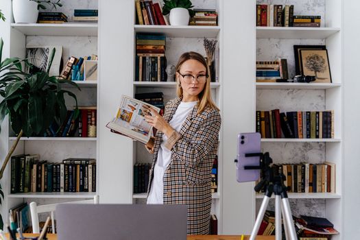 A woman recording a vlog in her home library, using a smartphone and tripod setup.