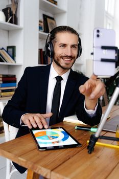 Smiling businessman in headphones using tablet for video call at office desk.