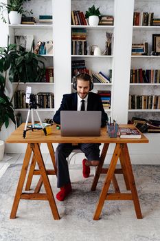 Man in a suit working remotely at home, using a laptop and headphones.