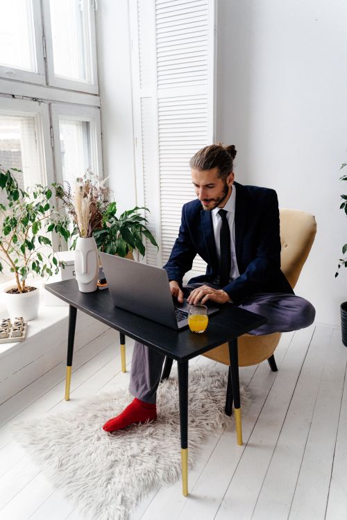 Free Man in suit working on laptop at home office with plants and natural light. Stock Photo