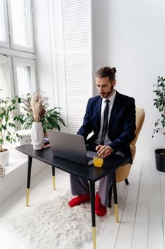 Businessman in a suit working remotely in a modern home office with a laptop and plants.