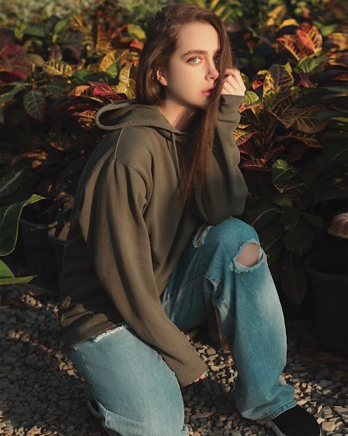 A Woman in Green Jacket and Blue Denim Jeans Sitting on Ground