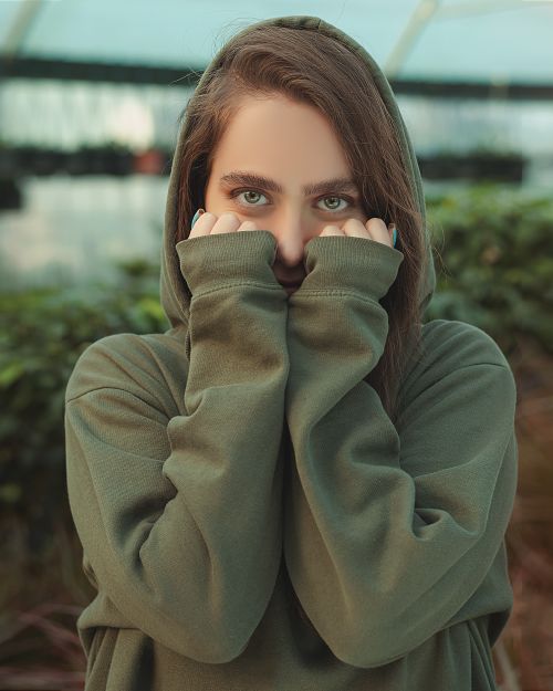 Free Young woman in green hoodie posing outdoors, hands near face, serene expression. Stock Photo