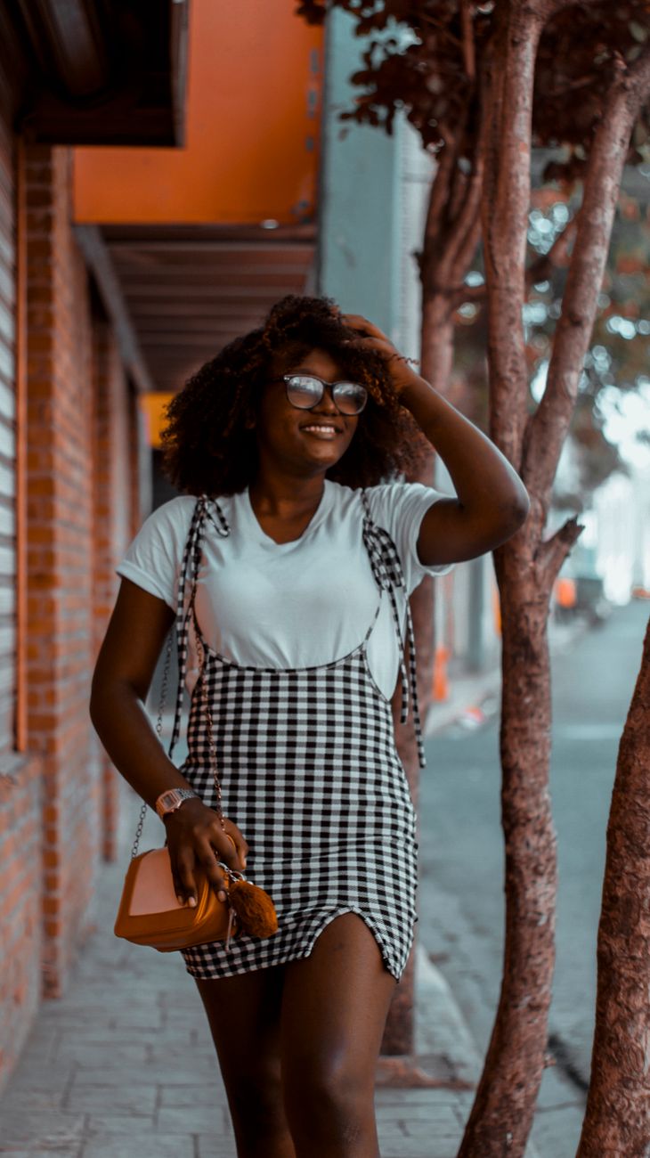 Uma mulher sorridente em um vestido xadrez estiloso caminhando ao ar livre.