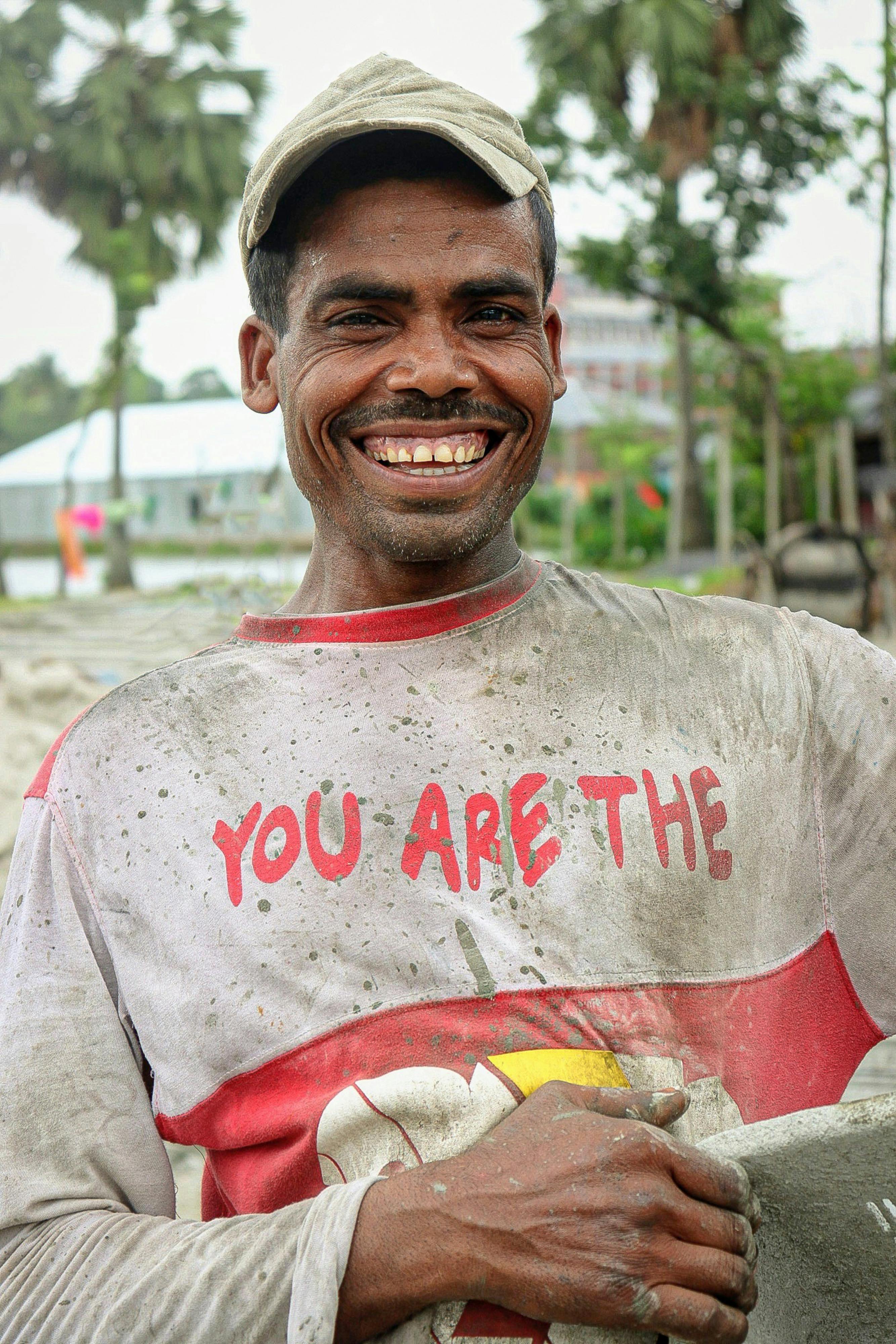 Smiling ethnic man in dirty clothes working on sandy seashore