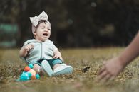 Little girl in casual wear yelling loudly and crying while sitting on grassy lawn in park