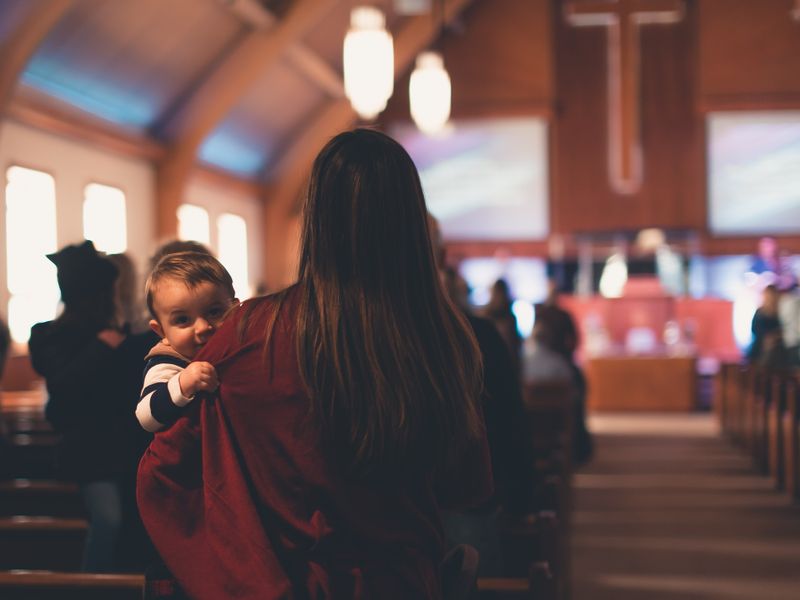 Woman carrying a child inside a church with people worshipping in the background - historic churches