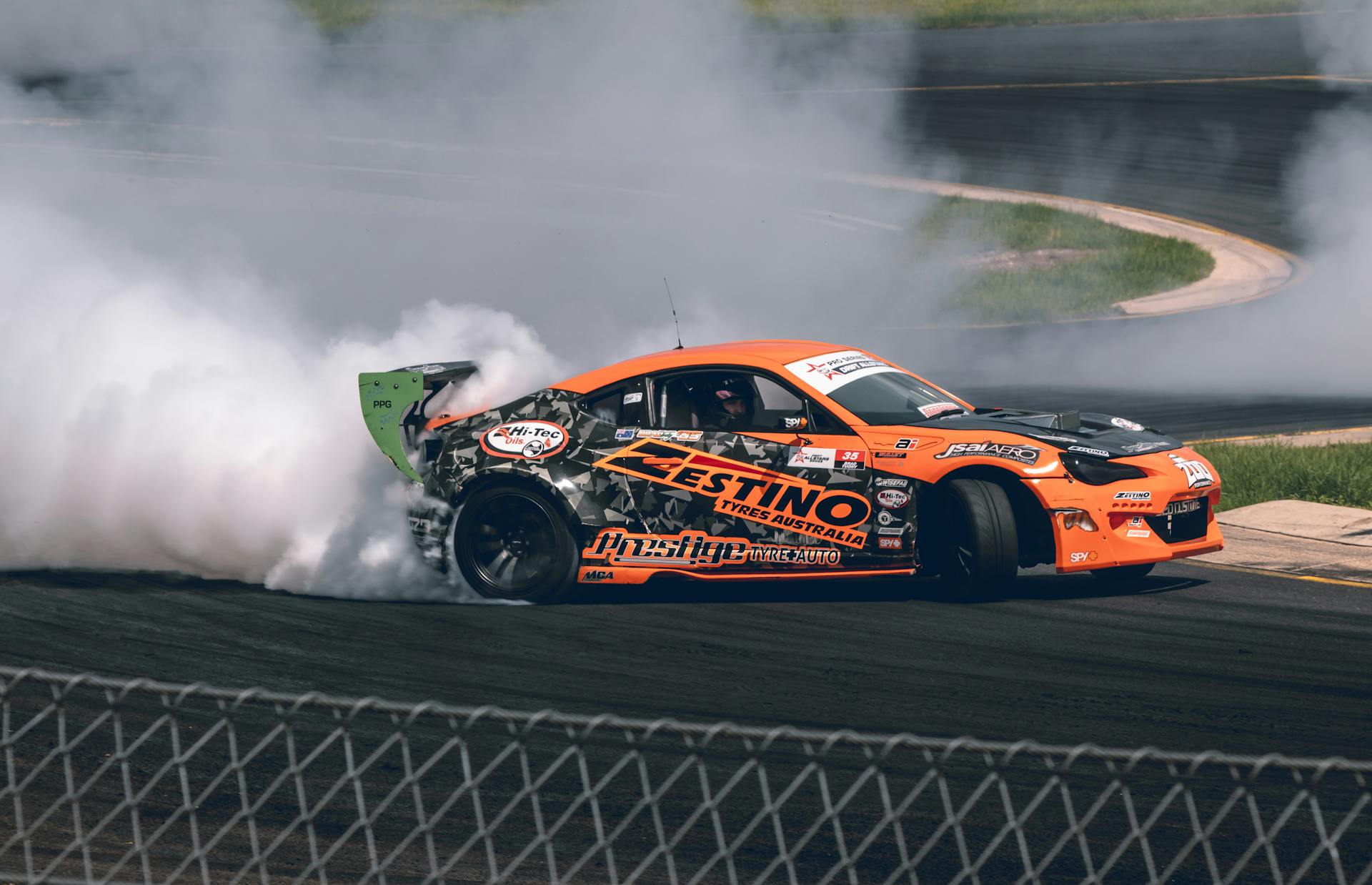 Orange drift car in action on a race track, producing smoke during a motorsport event in Australia.