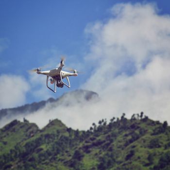 High-tech drone hovering above lush, fog-covered mountains with a clear blue sky.