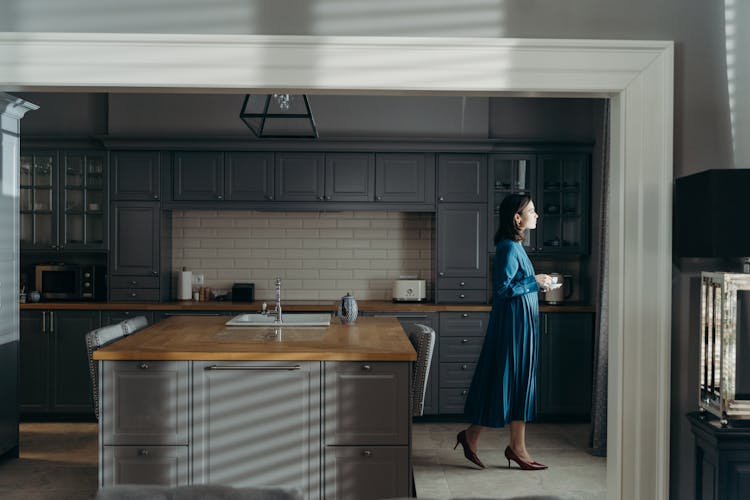 Woman In A Blue Dress In A Kitchen With Gray Wooden Cabinets