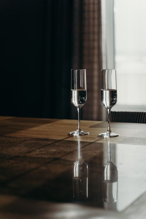 Free Two crystal champagne glasses with bubbly liquid elegantly displayed on a sunlit wooden table. Stock Photo