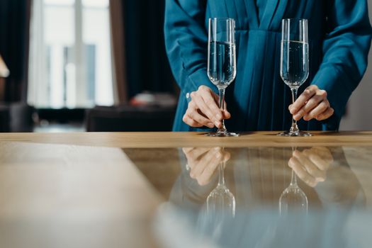 Person in blue attire elegantly setting champagne glasses on a table indoors.