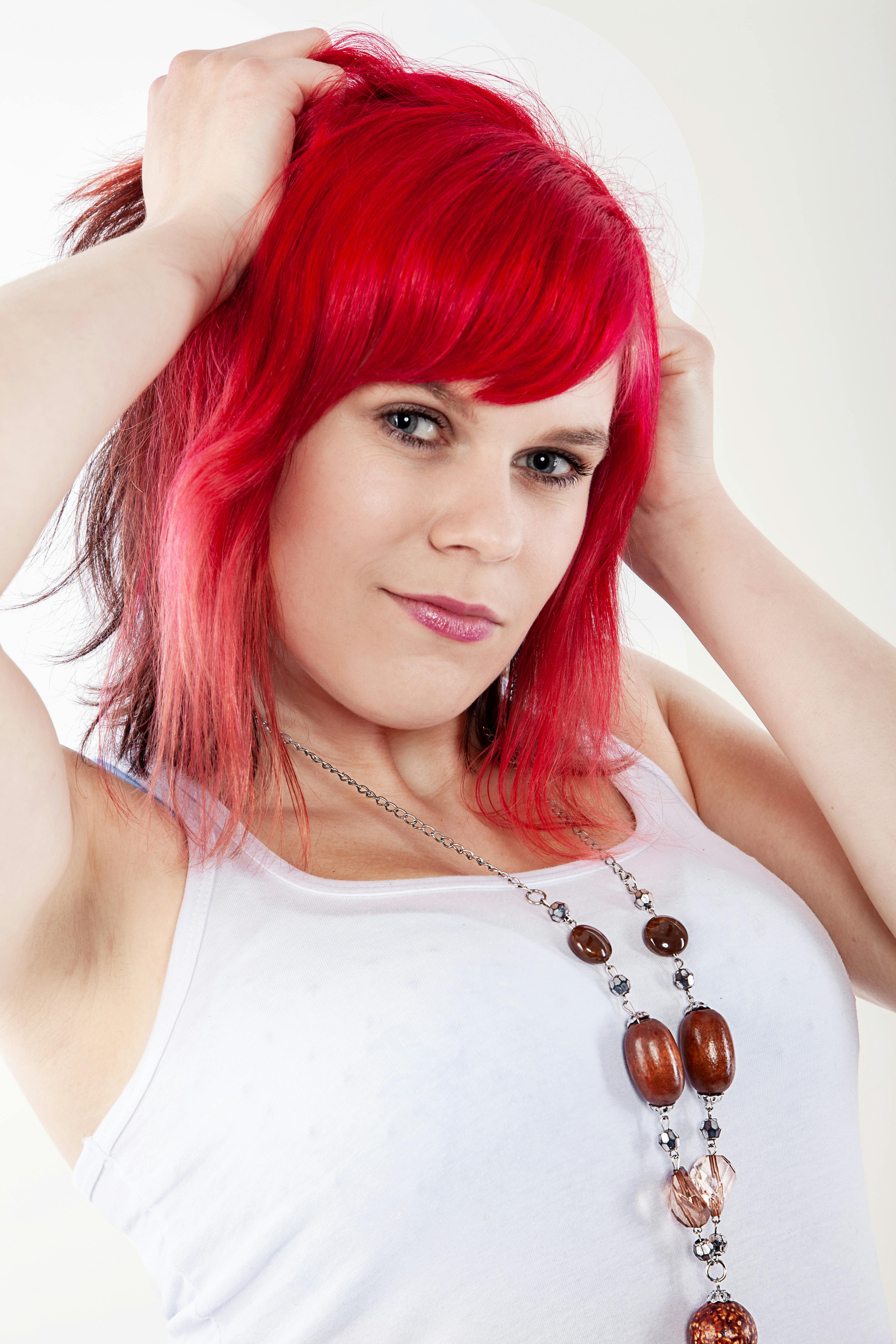 Woman with red hair in white tank top posing confidently indoors.