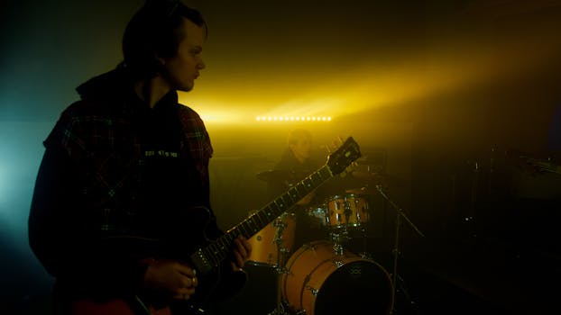 Musicians performing with guitars and drums under dramatic stage lighting.
