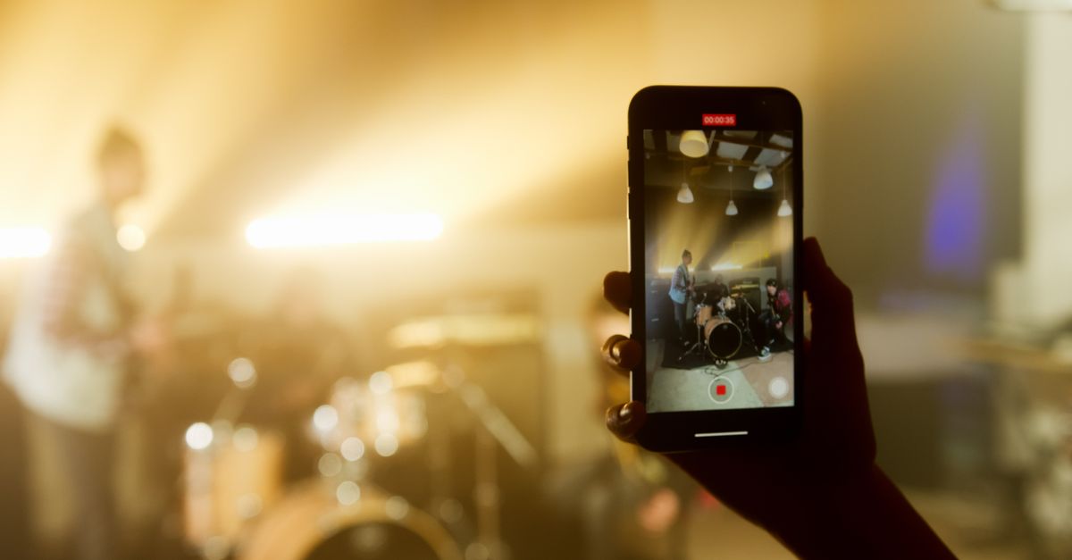 A smartphone captures a live band performance in a warm, atmospheric setting.