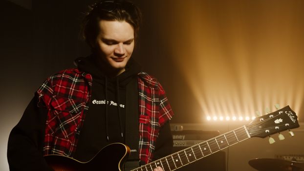 Young male musician playing electric guitar on stage with warm lighting.