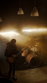 Live band performance featuring a guitarist and drummer on stage with vibrant lighting effects.