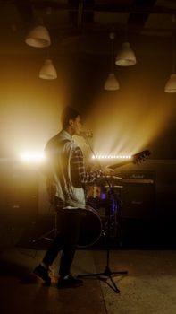 Solo guitarist performing onstage with dramatic lighting and musical equipment in the background.