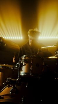 A drummer energetically playing a drum set under vibrant stage lights, capturing the essence of live music performance.