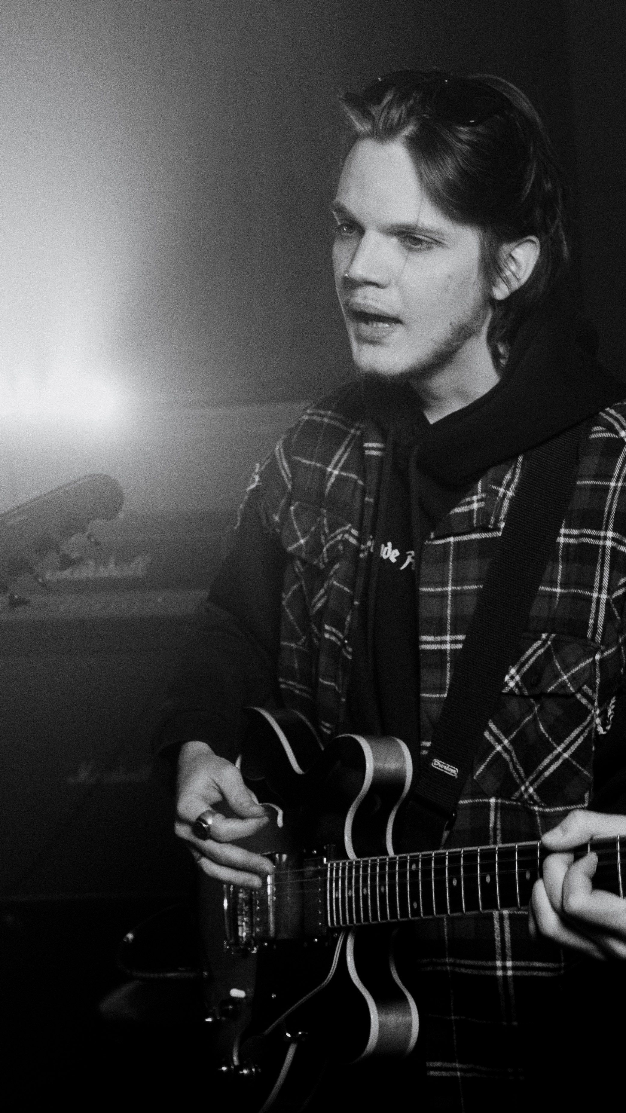 Monochrome image of a young male musician passionately playing an electric guitar indoors.