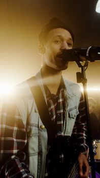 A male musician passionately sings into a microphone during a live performance with a vibrant stage setup.