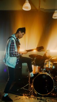 Energetic live band performance with a guitarist and drummer on stage under vibrant lighting.