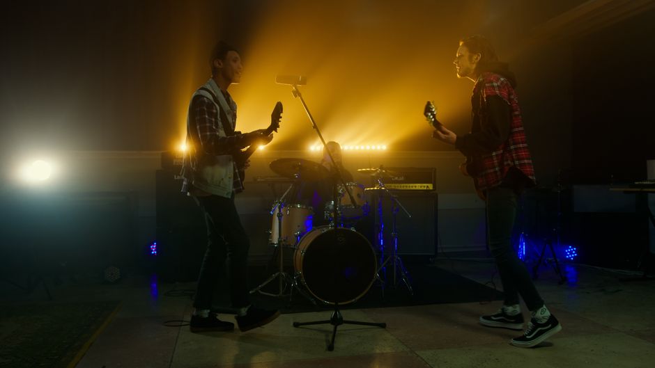 A dynamic live band performance with guitarists and drummer under vivid stage lighting.