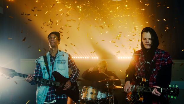 Energetic live band performance with confetti shower, featuring guitars and drums.