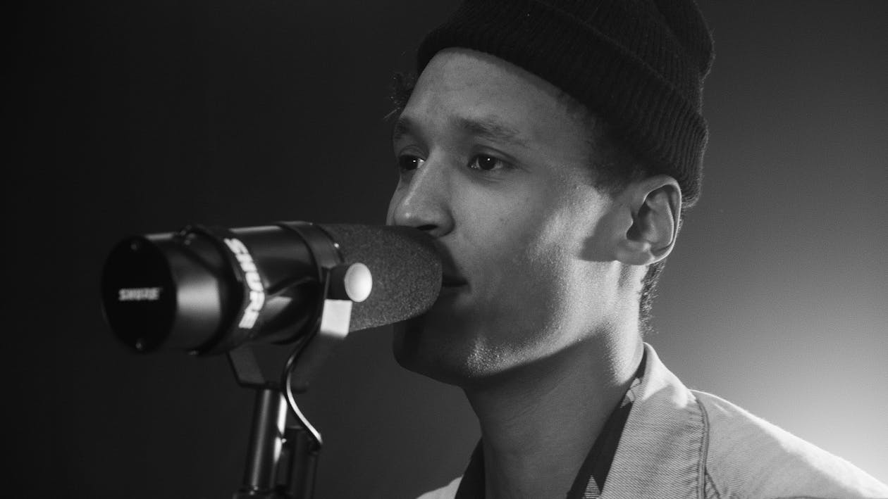 Grayscale Photo of a Man with a Beanie Singing on a Microphone
