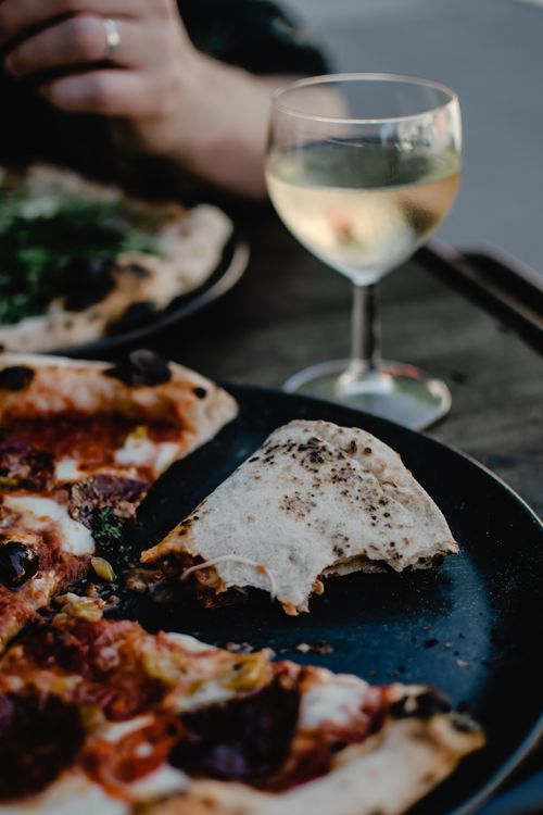 Free Close-up of artisan pizza and white wine on a table outdoors, creating a relaxing dining atmosphere. Stock Photo