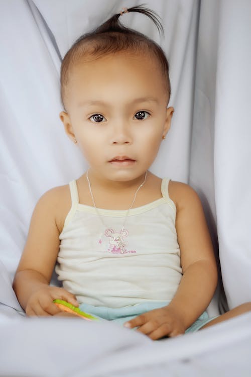 Cute baby girl sitting on white sheets with rattle