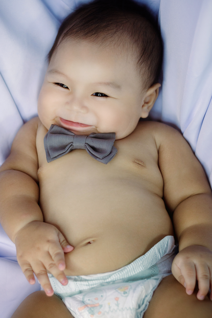 Fotomural Encantador bebé niño con pajarita, acostado en la cama con una gran sonrisa. Perfecto para temas de paternidad.