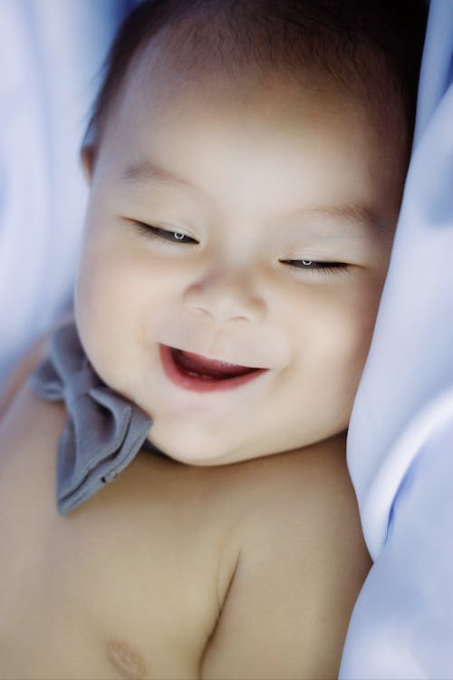Free Crop cute little Asian baby boy wearing blue bow tie laughing while lying on white plaid and looking away Stock Photo