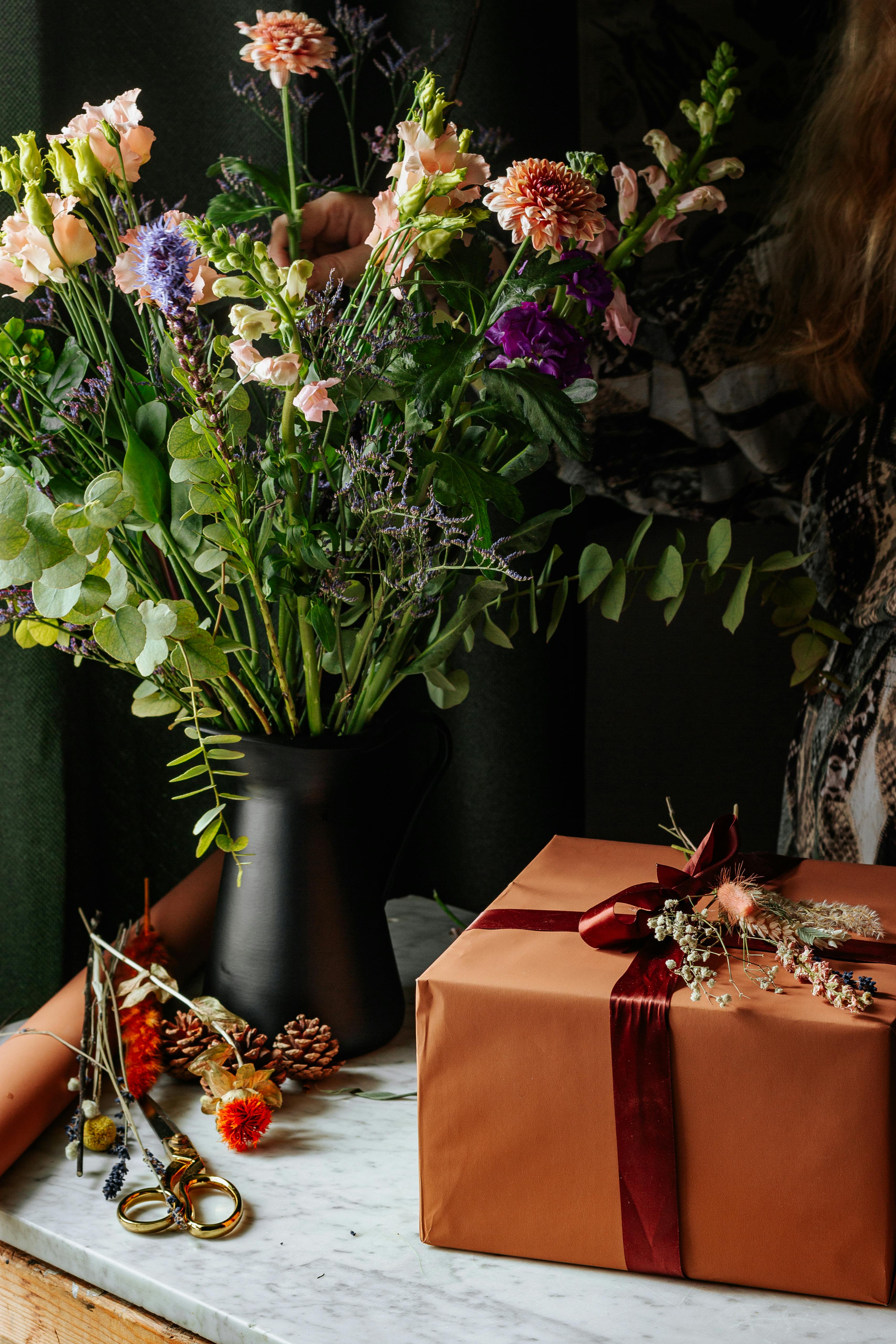 Stylish floral bouquet in a black vase with a wrapped gift on marble. Perfect for celebrations and decor.