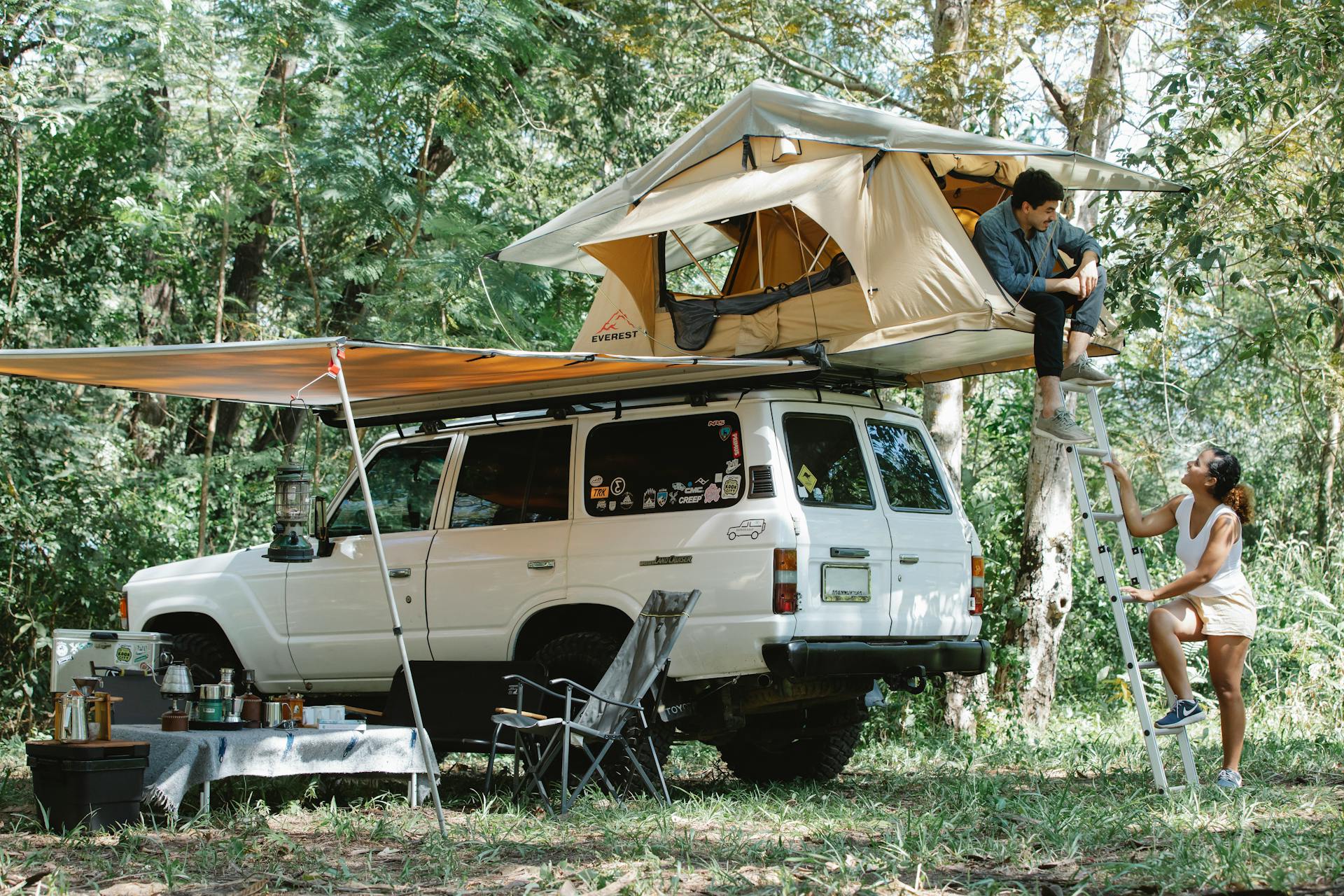 A couple camping with a rooftop tent on an SUV in a lush forest, enjoying nature and adventure.