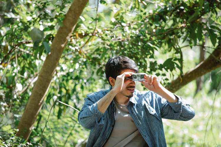 Focused Young Guy Using Small Binoculars In Woods