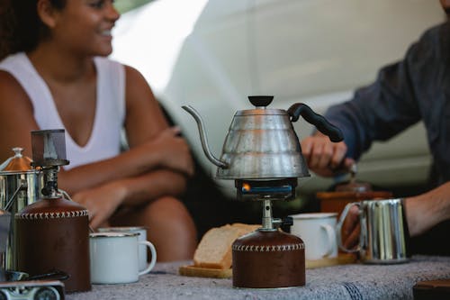 Crop friends preparing coffee and boiling kettle on gas stove