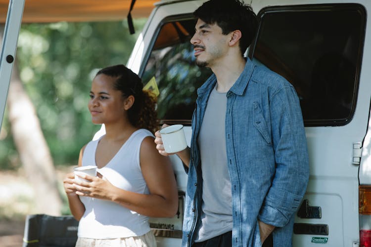 Dreamy Diverse Couple With Cups Of Coffee Standing Near Car