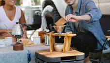 Crop smiling couple wearing casual outfits preparing aromatic pour over coffee during picnic on sunny day
