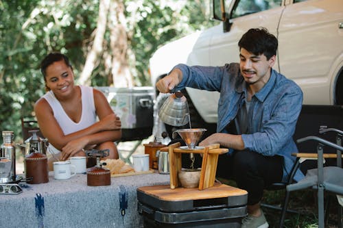Happy diverse couple preparing pour over coffee in campsite