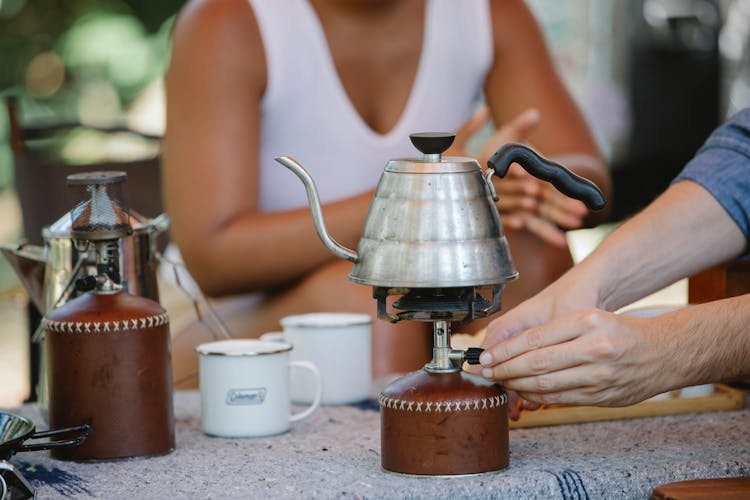 Crop Couple Heating Metal Kettle On Camp Stove