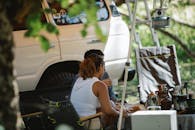 Side view of unrecognizable couple sitting at table near SUV car and drinking coffee during road trip in nature on sunny summer day