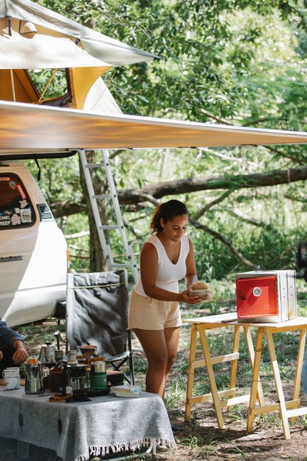 A tidy campsite gear layout on a picnic table with cookware, a lantern, and storage bins at golden hour