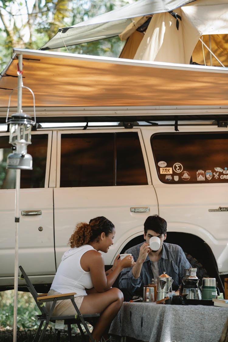 Anonymous Diverse Couple Drinking Coffee Near Off Road Vehicle In Park