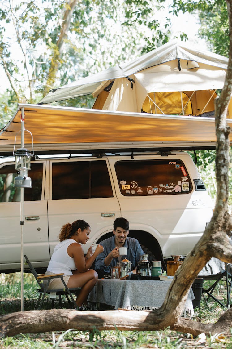 Positive Young Diverse Couple Resting Under Tent During Weekend In Nature