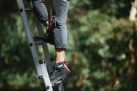 Faceless camper climbing ladder in forest