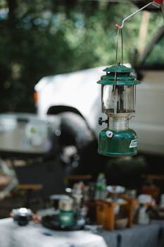 Retro green camping lantern with blurred off-road vehicle in a forest setting.